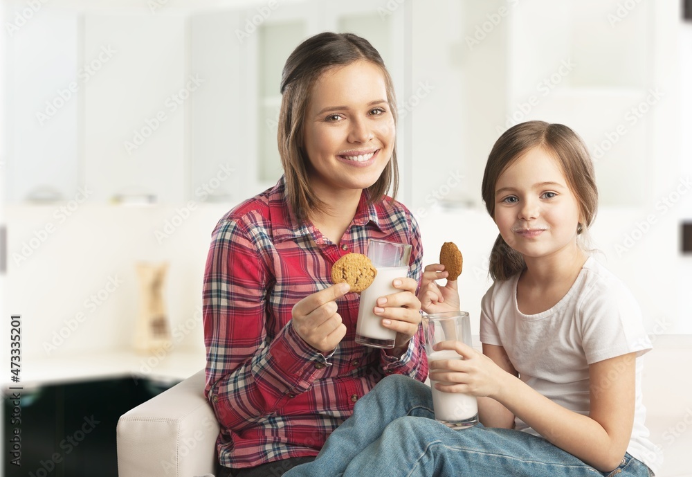 Pretty girl drinking milk with her mom and eating cookies, sitting at the kitchen