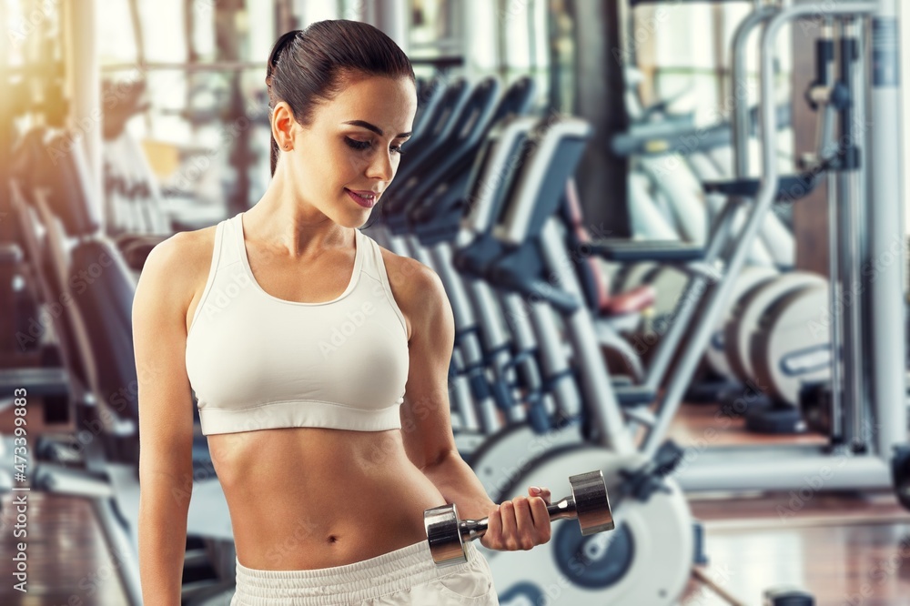 Workout in gym by a beautiful woman using dumbbell. Sport woman warm up before a workout.