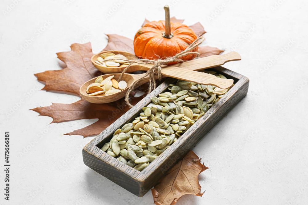 Wooden board and spoons with pumpkin seeds on white background