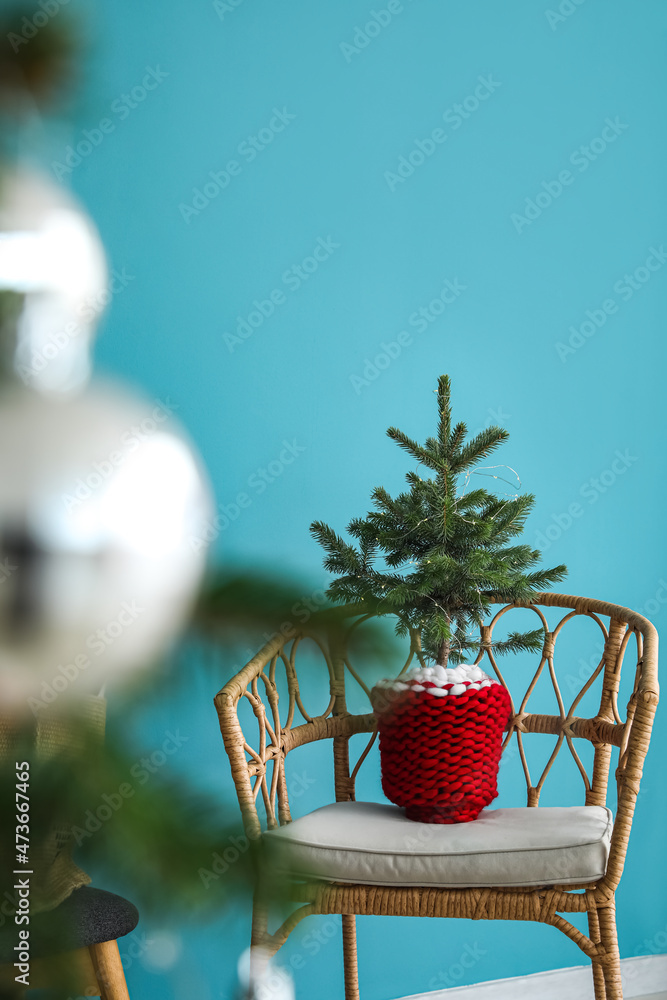 Christmas tree with glowing lights in armchair near color wall