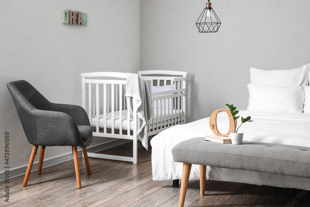 Interior of light bedroom with white crib and armchair