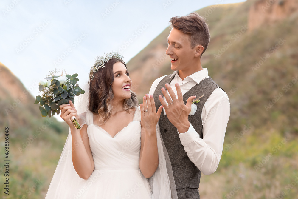 Happy newlyweds showing their wedding rings outdoors