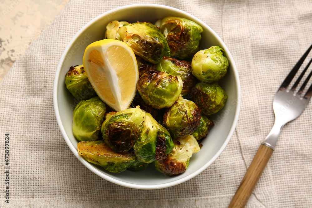 Bowl with tasty roasted Brussels cabbage and lemon on table