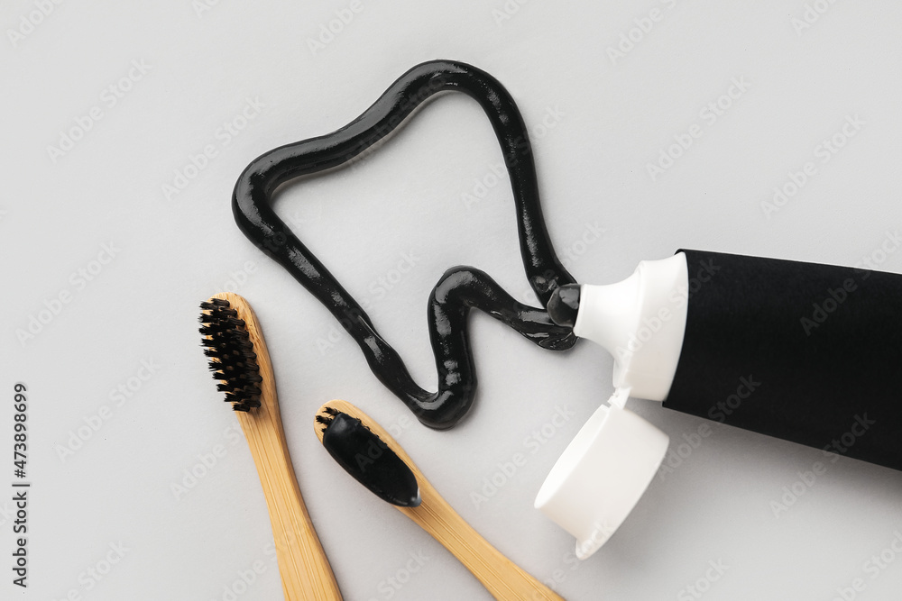 Tooth made of black paste, bamboo brushes and tube on light background