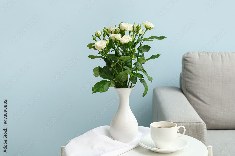 Vase with beautiful bouquet of roses and cup of coffee on table in room