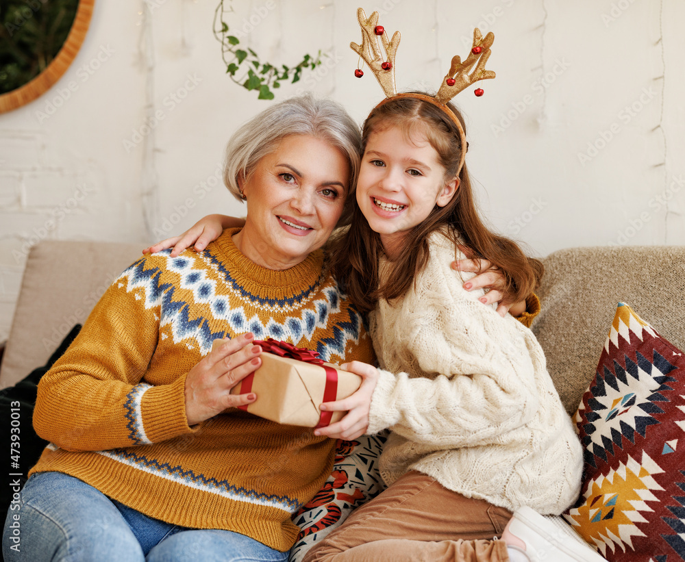 Little girl granddaughter giving Christmas gift box to smiling grandmother during winter holidays