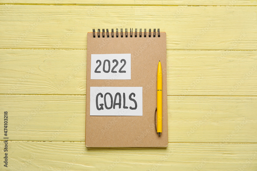 Pen and notepad with text 2022 GOALS on color wooden background