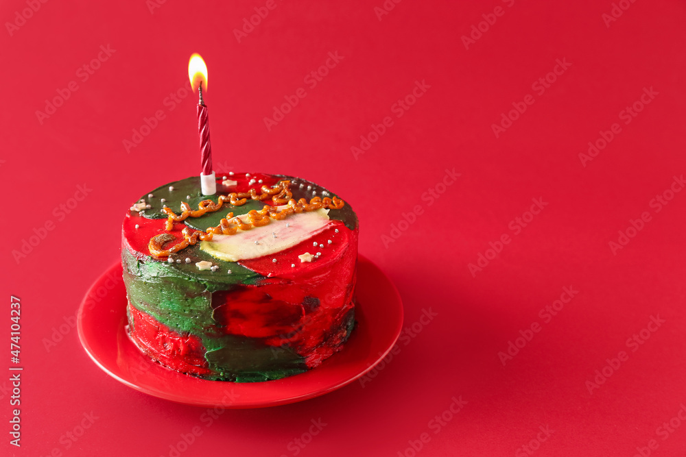 Plate with Christmas bento cake and candle on red background