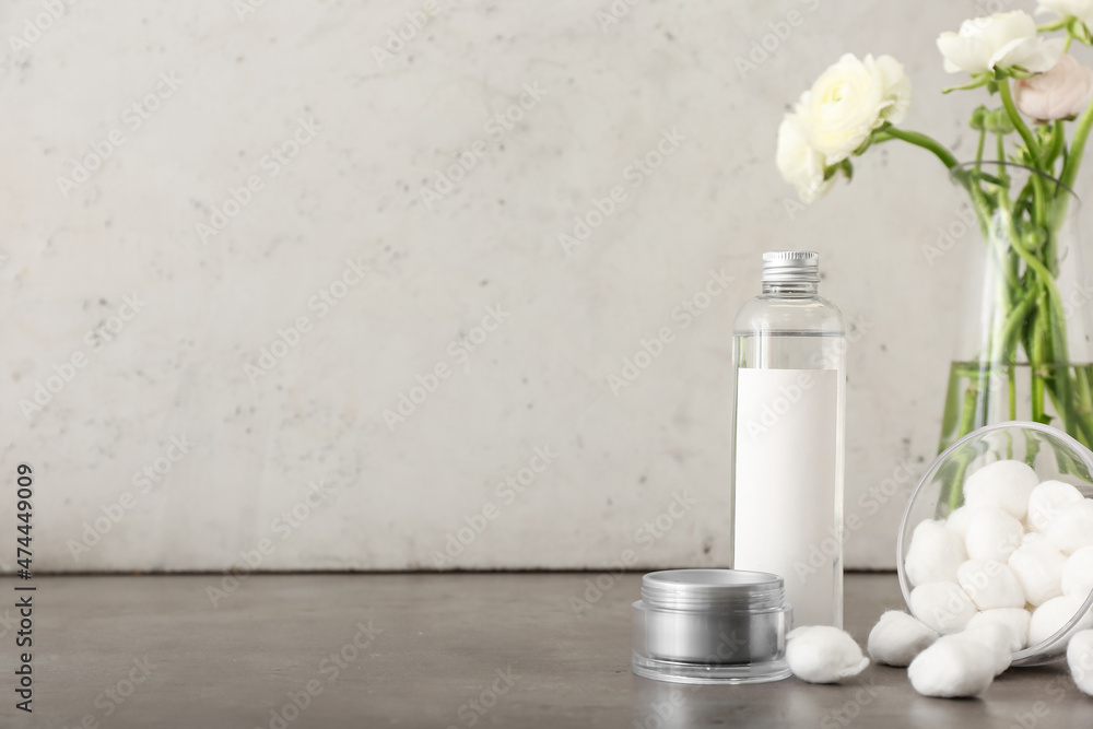 Bottle with cosmetics, jar with face cream and vase with ranunculus flowers on grey table