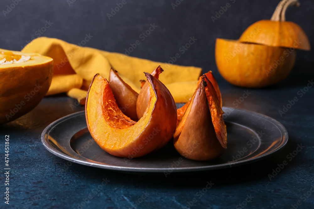 Plate with baked pumpkin pieces on black background