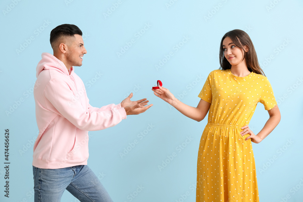 Young woman proposing to her happy boyfriend on color background