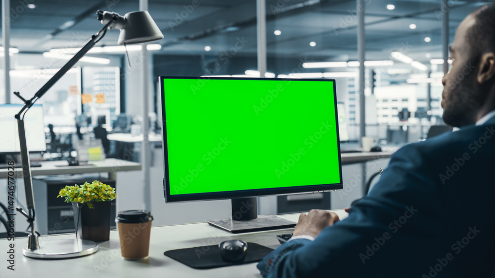 Successful Black Businessman Sitting at Desk Working on Green Screen Laptop Computer in Office. Afri