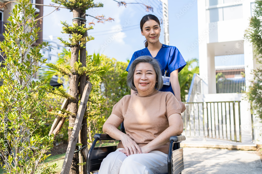 坐在绿色公园轮椅上的亚洲快乐老年女性患者。