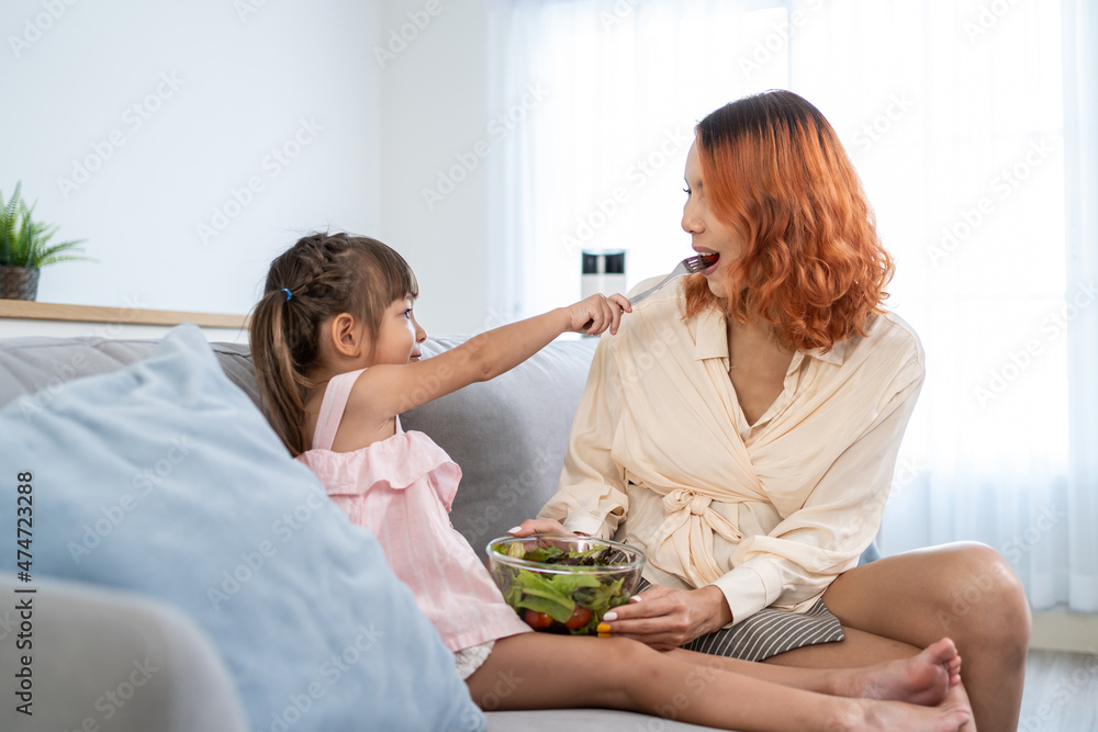 亚洲年轻快乐的孩子女儿在家里喂漂亮的妈妈绿色沙拉