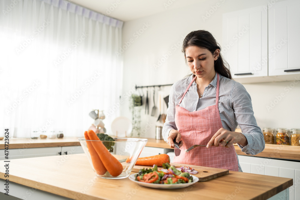 爱高加索的女人穿着围裙在家里的厨房里做绿色沙拉。