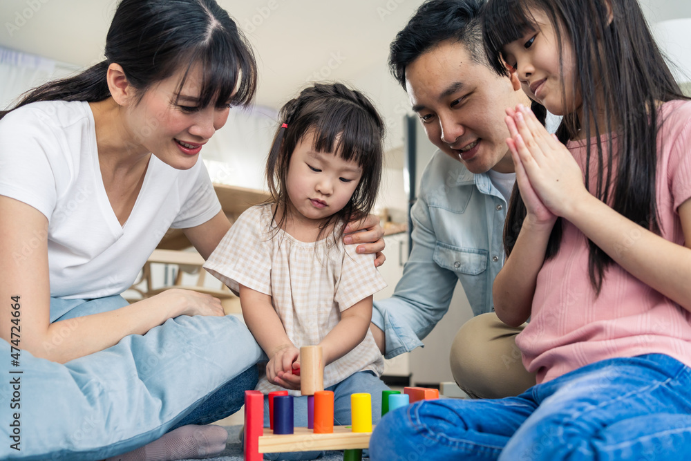 Asian happy family sit on floor, play kid toy together in living room.