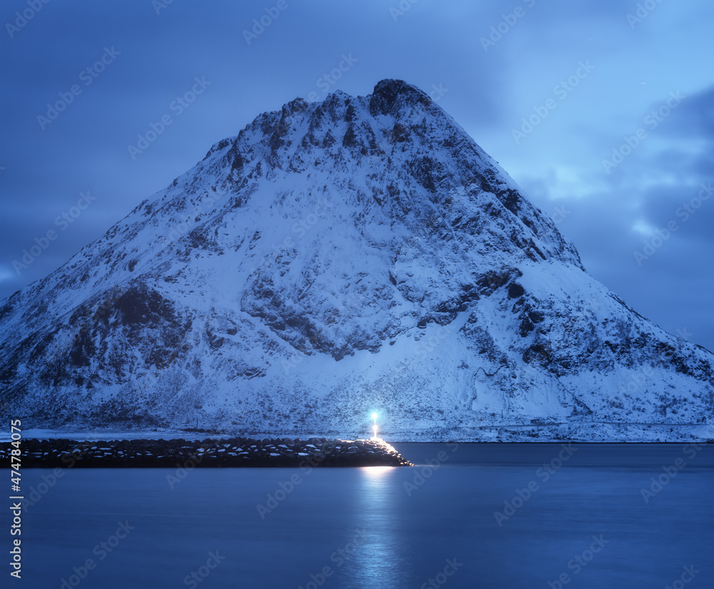 灯塔、大海和美丽的雪山，黄昏时多云的蓝天映在水中。