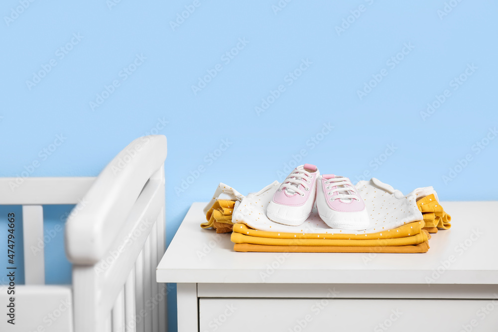 Stack of baby clothes and shoes on shelf near blue wall