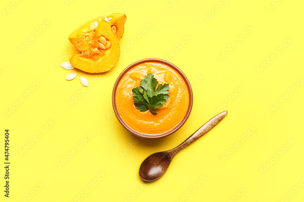 Bowl of tasty pumpkin cream soup and spoon on yellow background