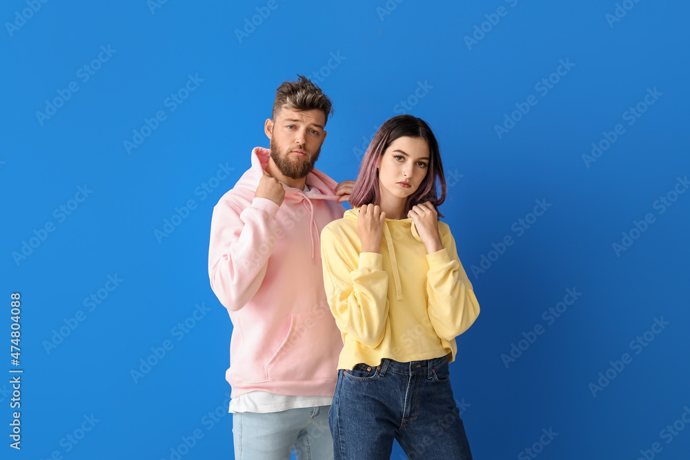 Cool young couple in hoodies on color background