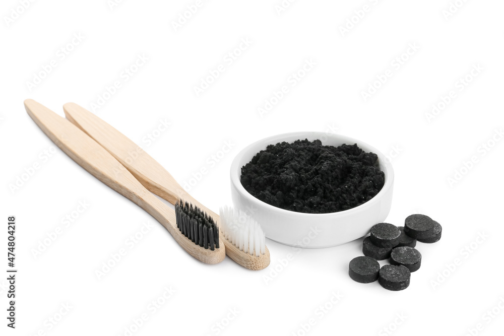 Bowl with activated charcoal tooth powder, pills and brushes on white background