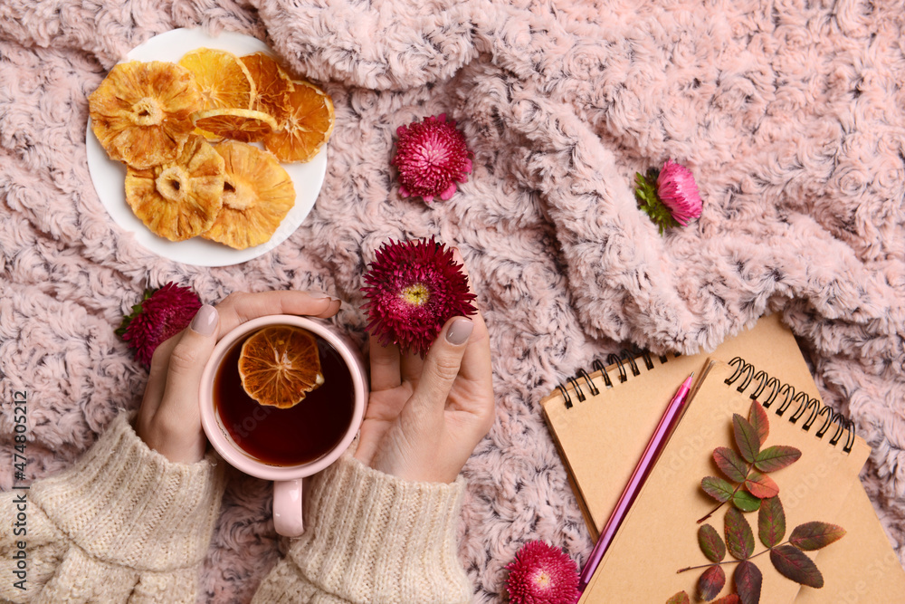 织物背景上有一杯茶、干果和鲜花的女性手