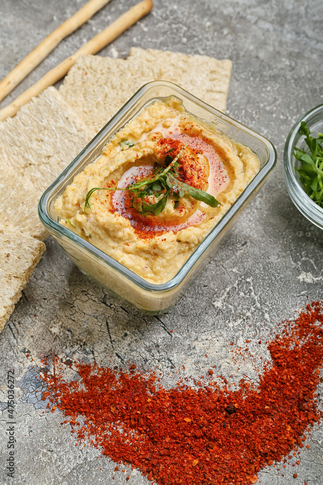 Bowl with delicious hummus and spices on grey background, closeup