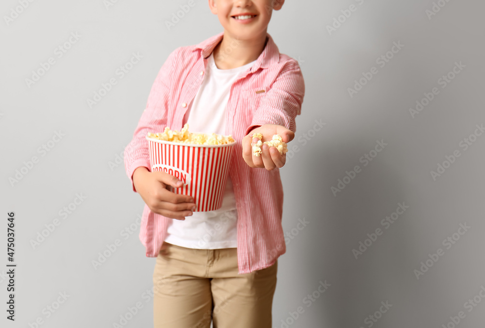 Little boy with bucket of tasty popcorn on light background