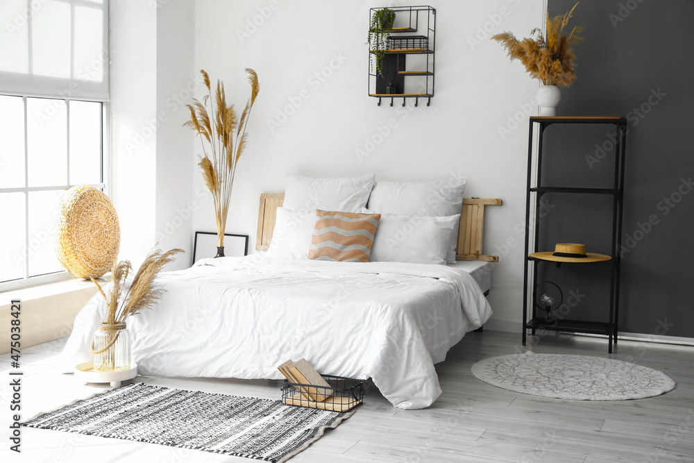 Interior of modern bedroom with dry reeds in vases and shelving unit