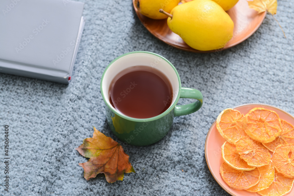 Green cup of hot tea and fallen leaf and food on grey fabric background, closeup