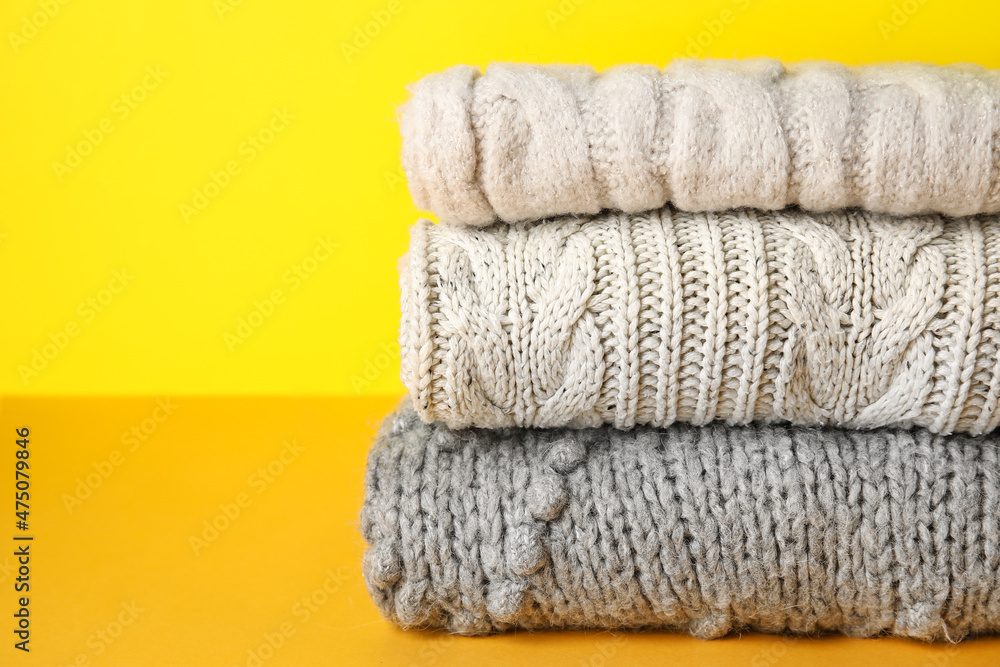 Stack of knitted sweaters on color background, closeup