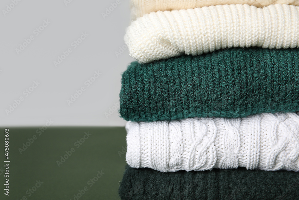 Stack of stylish knitted sweaters on color background, closeup