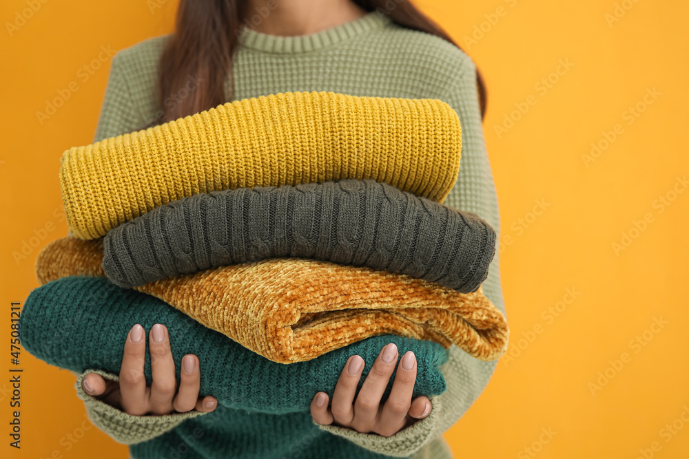 Woman with beautiful manicure holding stack of warm sweaters on color background