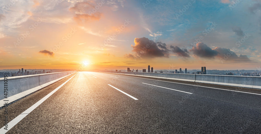 Empty asphalt road with modern city skyline and buildings at sunrise