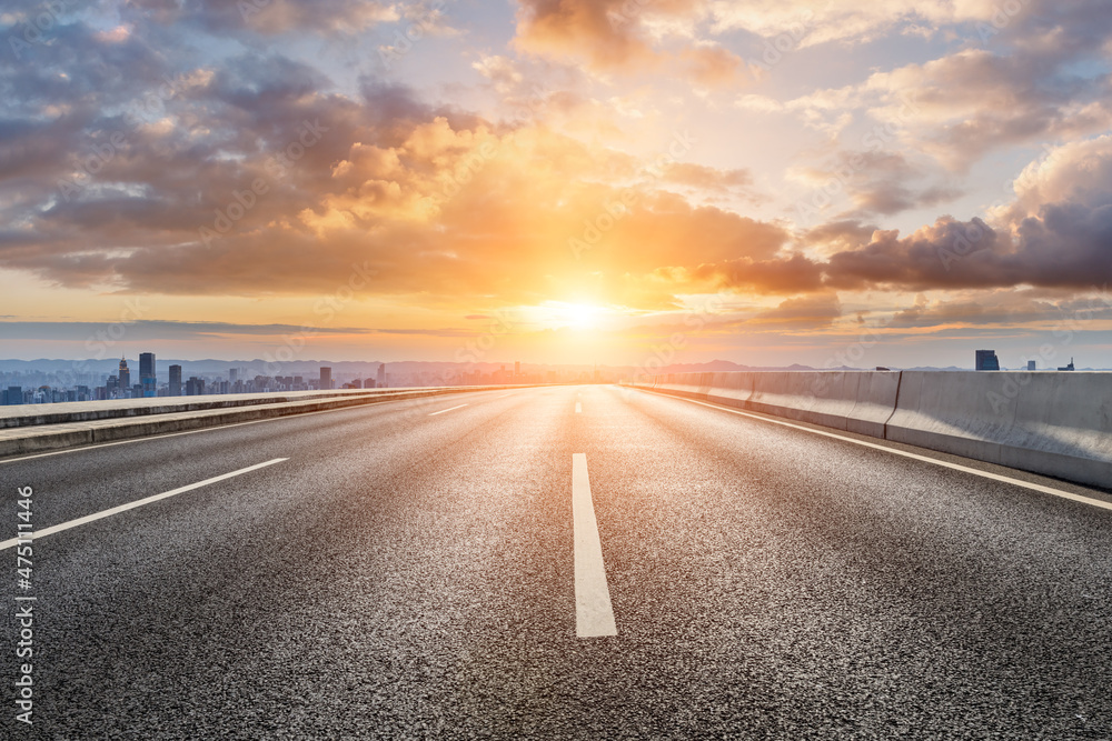 Empty asphalt road with modern city skyline and buildings at sunrise