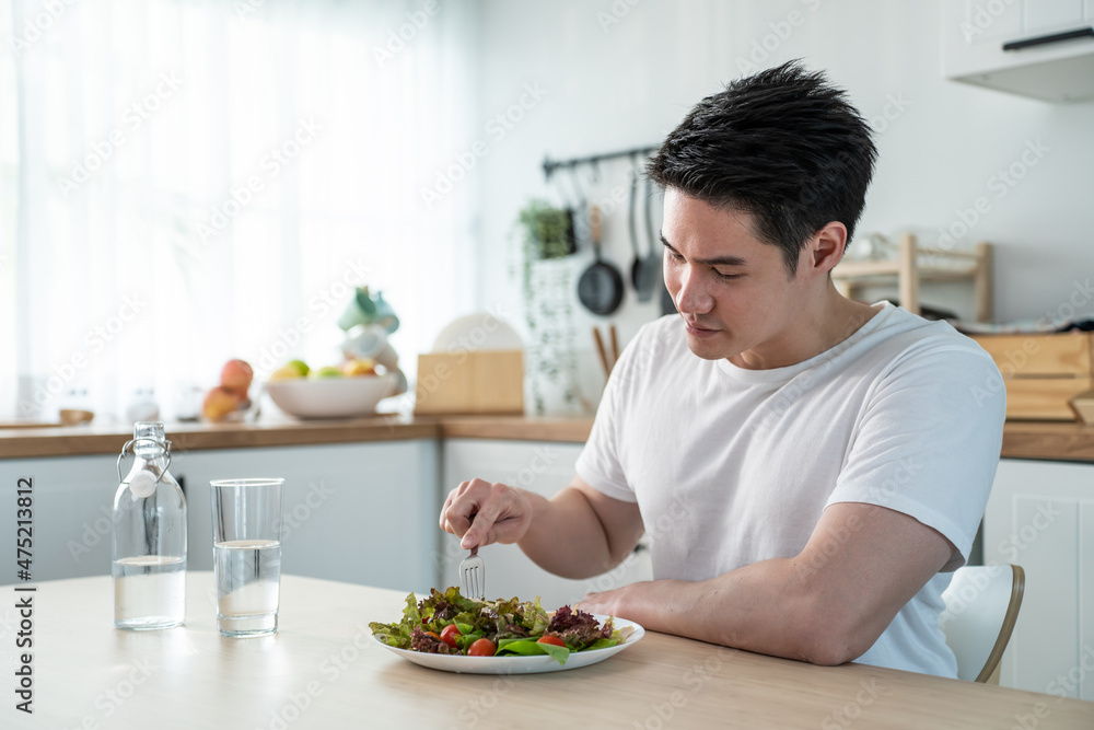 亚洲魅力英俊男性在家厨房吃绿色沙拉。