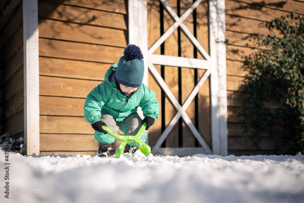 男孩在冬天玩雪。穿着绿色夹克，戴着针织帽的小孩在附近滚雪球