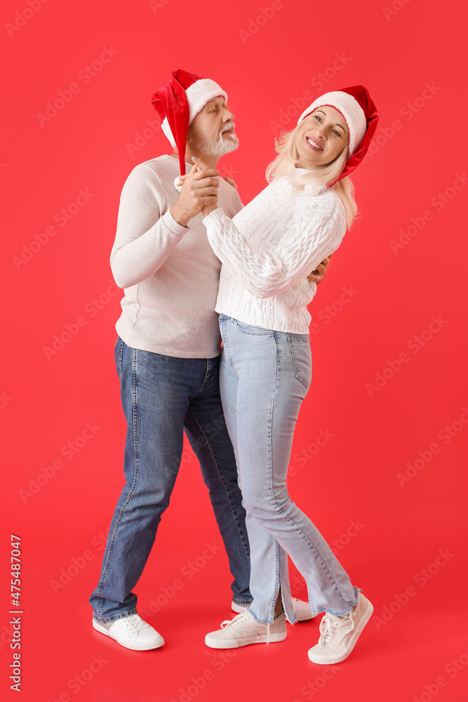 Happy dancing mature couple in Santa hats on color background