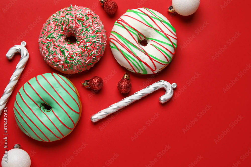 Tasty Christmas donuts with balls and candy canes on red background