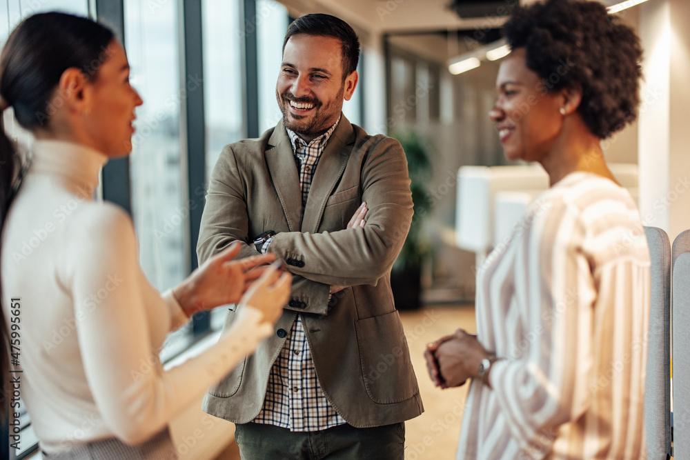 Three diverse colleagues, joking together in the office and laughing.