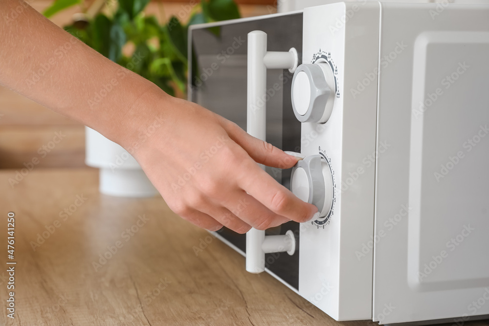 Woman switching on microwave oven in kitchen, closeup