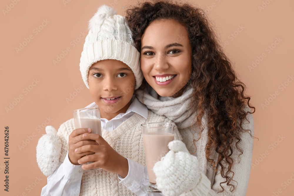 African-American boy and his mother in winter clothes and with tasty hot chocolate on color backgrou