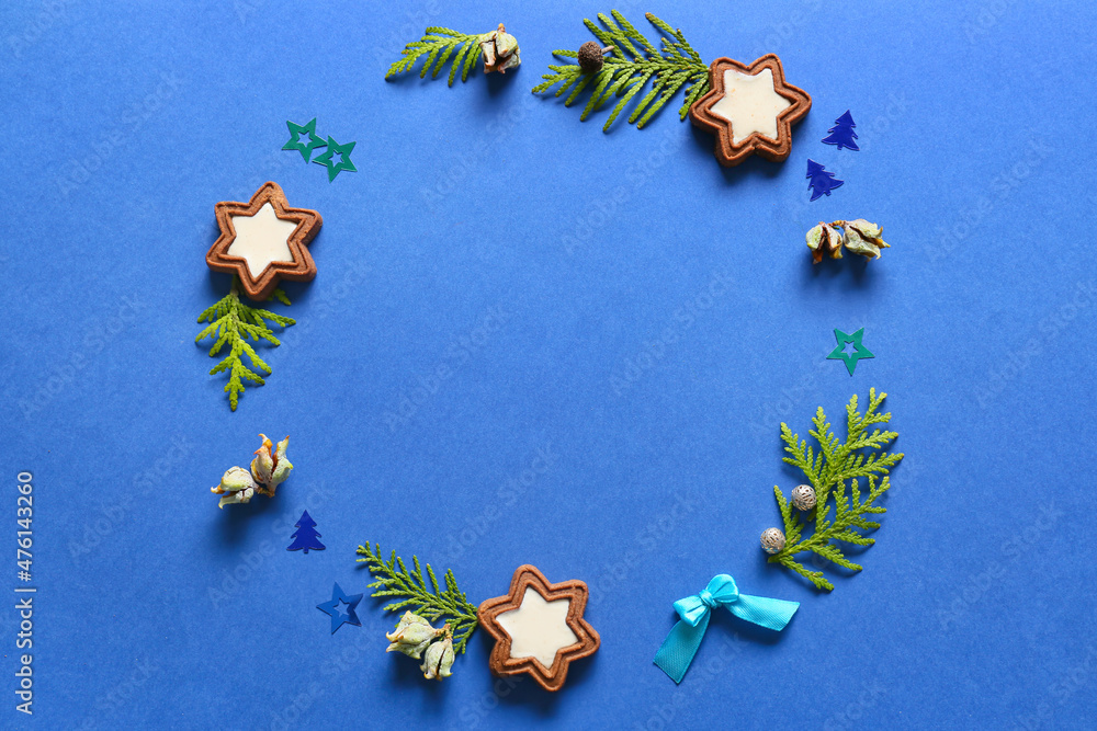 Frame made of fir branches and tasty cookies on blue background