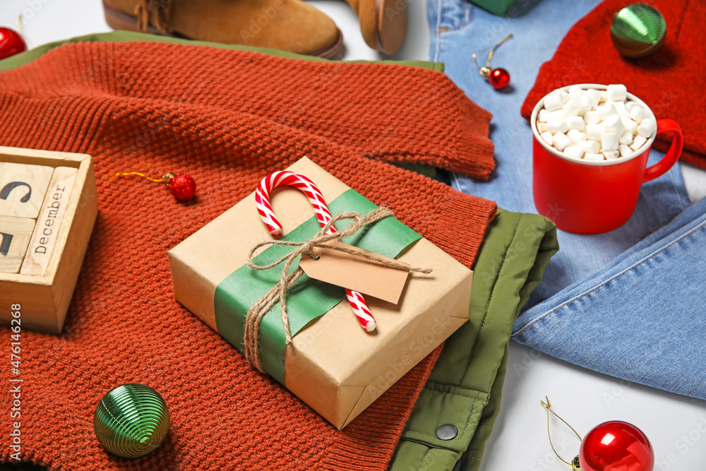 Set of childrens clothes and Christmas gift with cup of hot chocolate on light background