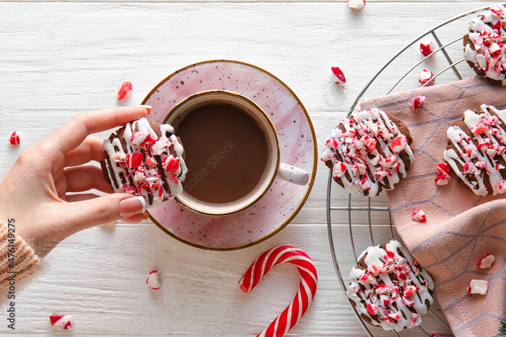 Woman drinking coffee with tasty candy cane cookies on white wooden background