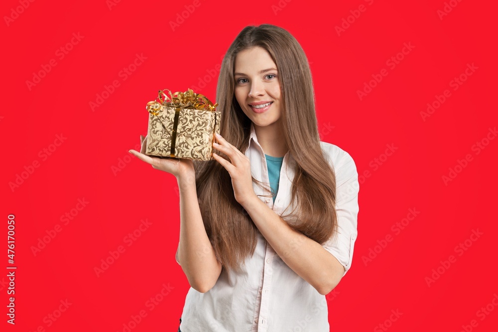 Pretty cheerful girl having fun holding in hands gift box on color background