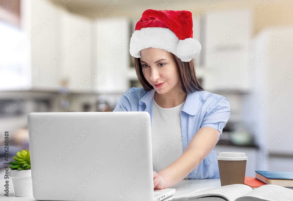 Smiling girl wearing Santa hat having video calling family by webcam. Woman with laptop sitting on k