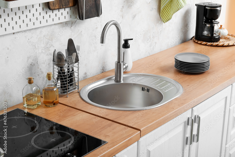 Wooden counter with silver sink and utensils near light wall in kitchen