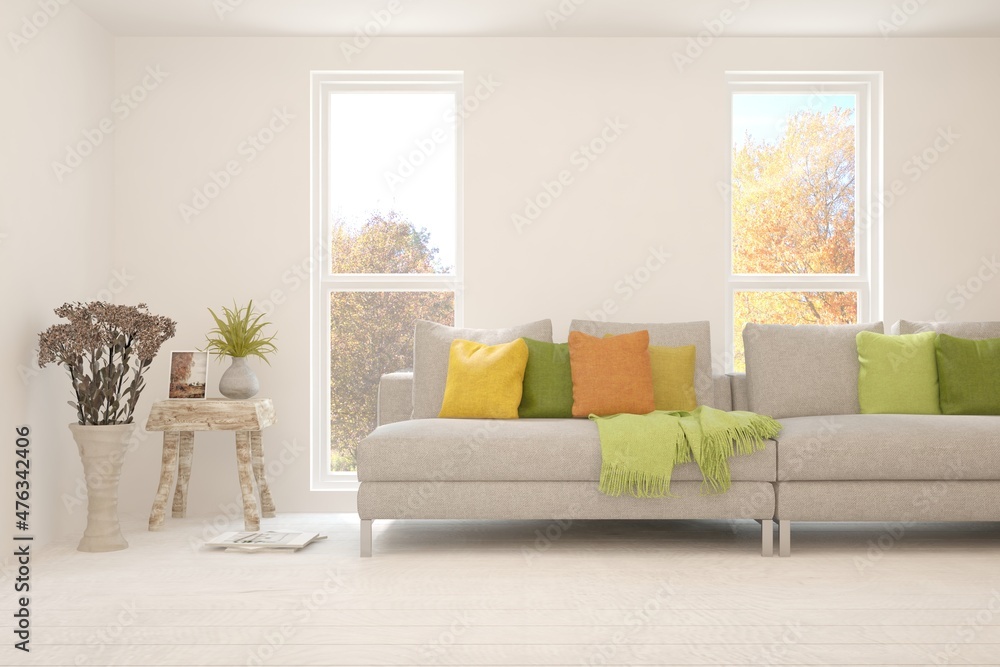 Stylish room in white color with sofa and autumn landscape in window. Scandinavian interior design. 