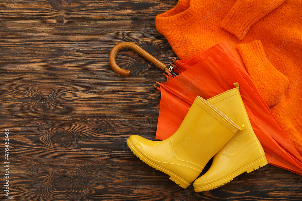 Umbrella, sweater and rubber boots on wooden background